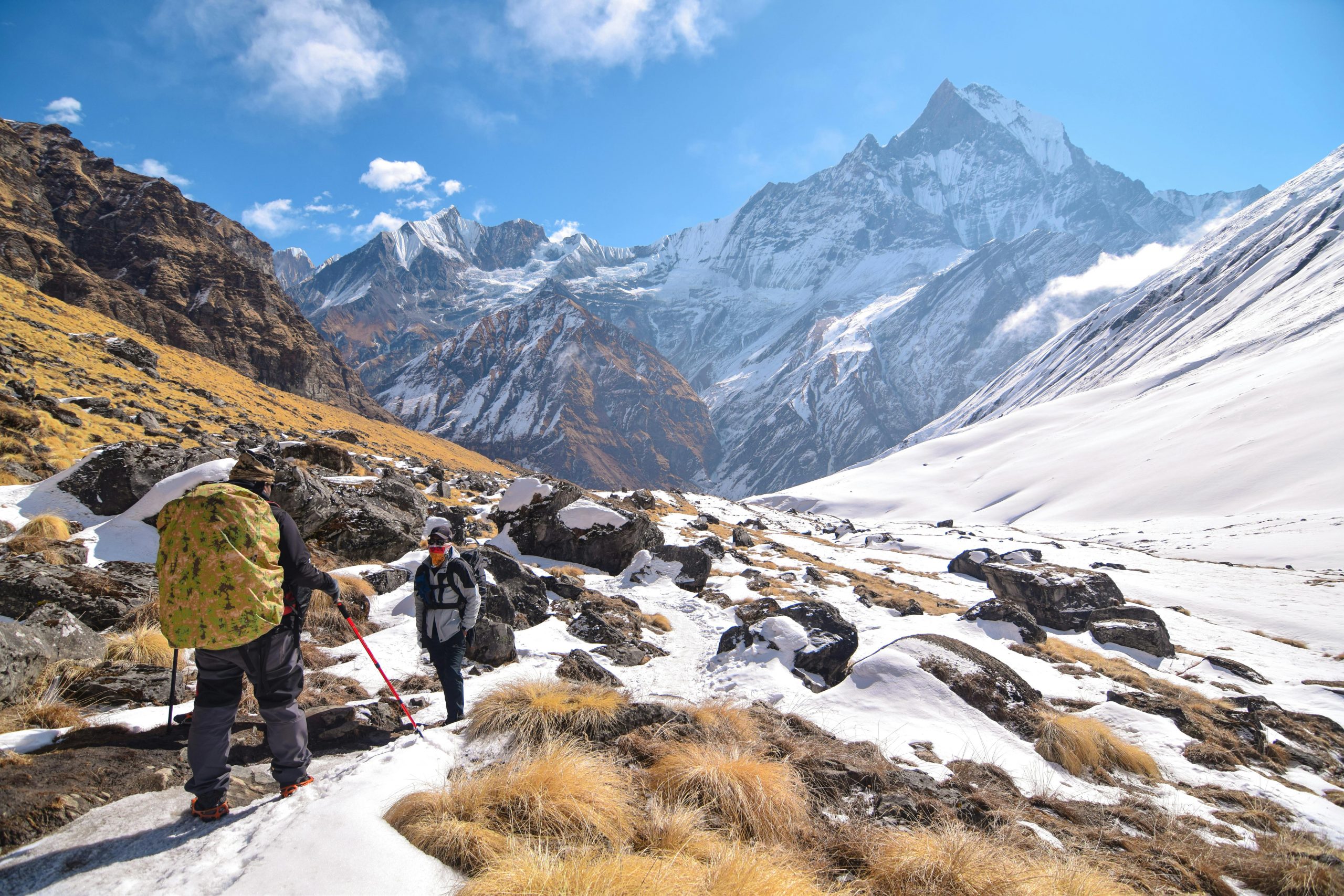 Two hikers trek through the snow-covered mountains of Khangsar, Nepal, under a vivid blue sky.